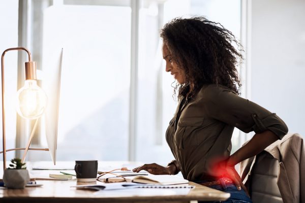 Shot of a businesswoman suffering from back pain while sitting at her desk